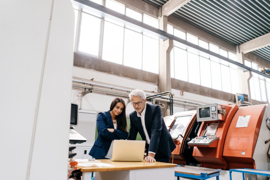 Businessman an woman in high tech enterprise, having a meeting, using laptop